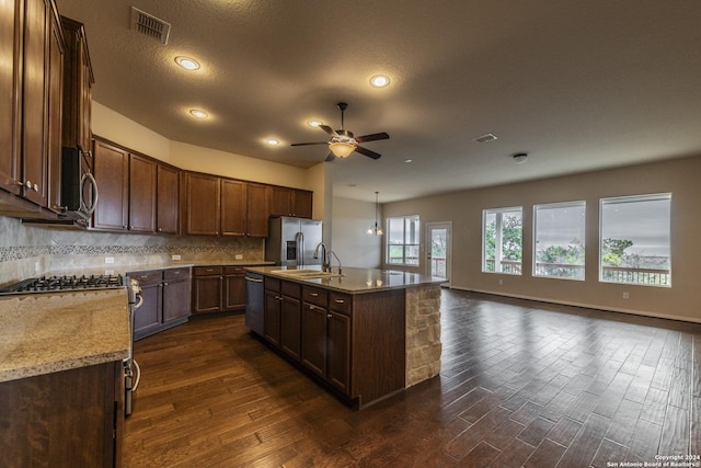 kitchen featuring a kitchen island with sink, dark hardwood / wood-style floors, a textured ceiling, light stone counters, and stainless steel appliances