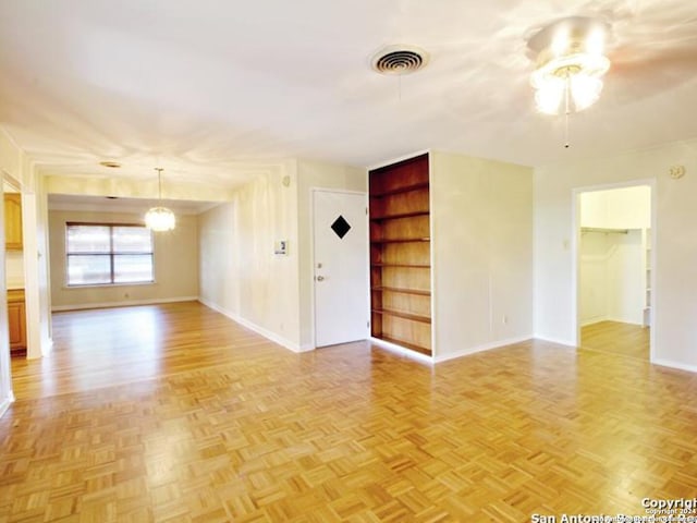 unfurnished room with built in shelves, ceiling fan with notable chandelier, and light parquet floors