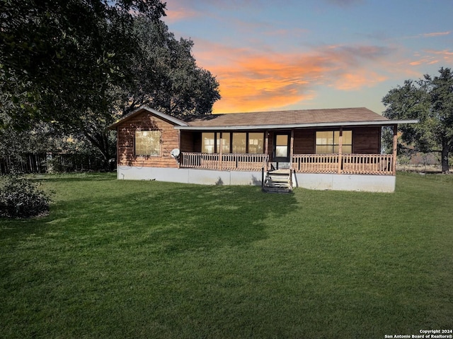 back house at dusk with covered porch and a yard