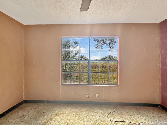 empty room with a wealth of natural light, ceiling fan, and a textured ceiling