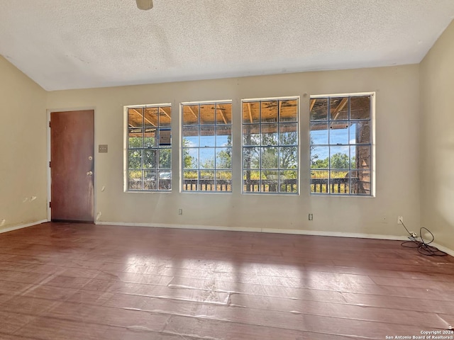 empty room featuring vaulted ceiling, wood-type flooring, and a textured ceiling