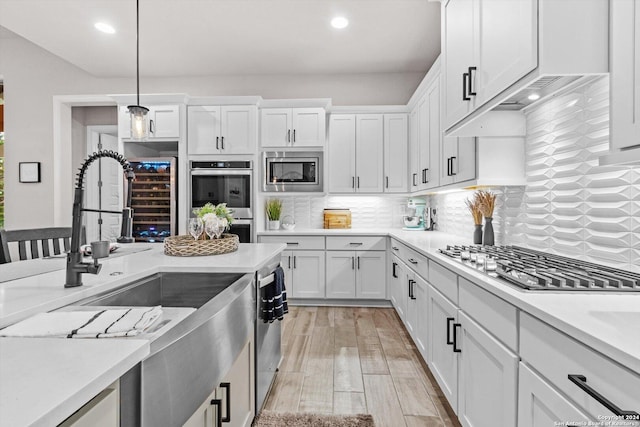 kitchen with appliances with stainless steel finishes, light wood-type flooring, white cabinetry, and hanging light fixtures