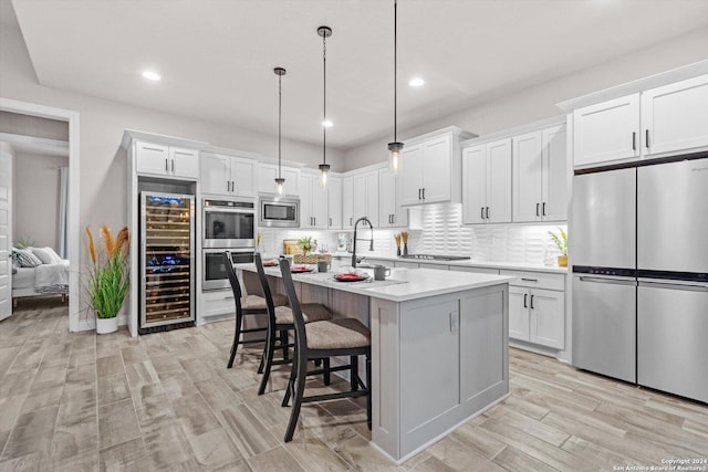 kitchen featuring wine cooler, an island with sink, decorative light fixtures, white cabinetry, and stainless steel appliances