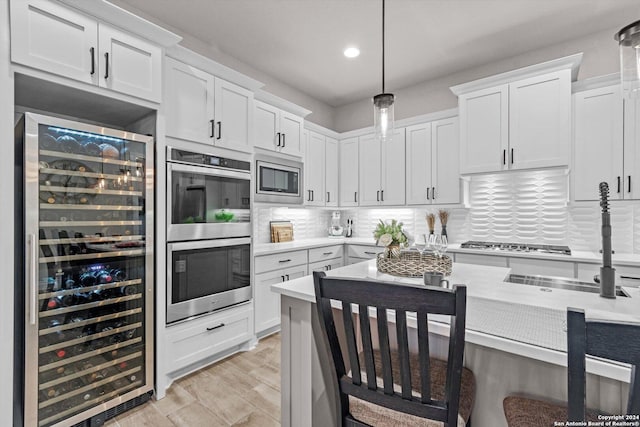 kitchen featuring white cabinets, hanging light fixtures, wine cooler, decorative backsplash, and appliances with stainless steel finishes