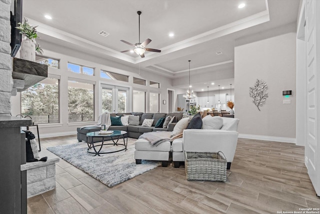 living room with ceiling fan with notable chandelier, a raised ceiling, light wood-type flooring, and ornamental molding