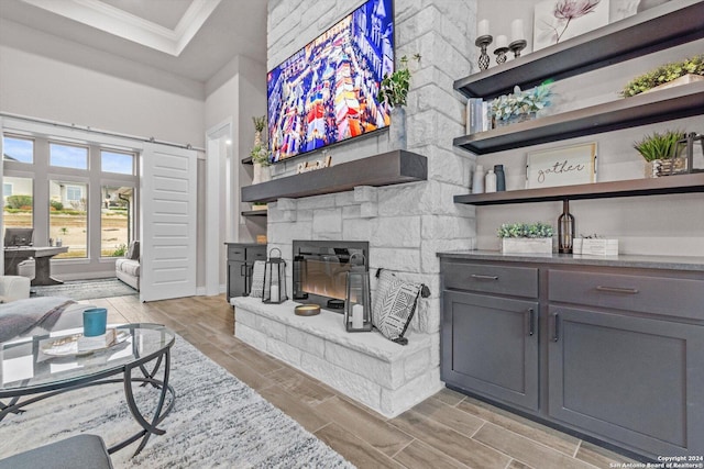 living room with light wood-type flooring, a stone fireplace, and crown molding