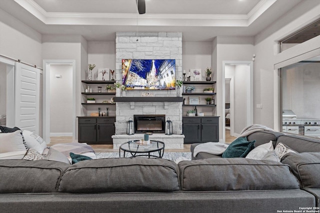 living room with ceiling fan, a stone fireplace, wood-type flooring, and ornamental molding