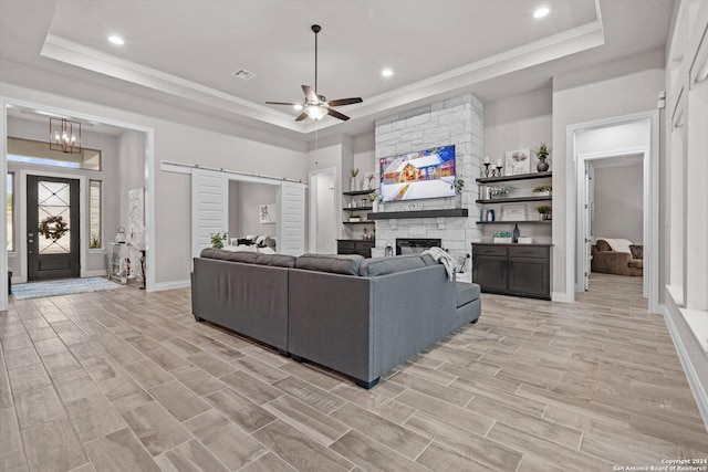 living room featuring a barn door, a tray ceiling, light hardwood / wood-style flooring, and a stone fireplace