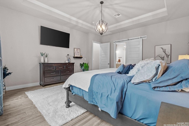 bedroom featuring a raised ceiling, a barn door, an inviting chandelier, and light wood-type flooring