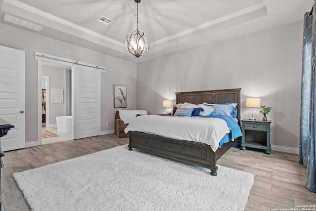 bedroom featuring a tray ceiling, a barn door, ensuite bathroom, and light hardwood / wood-style floors