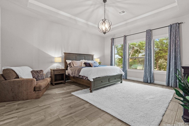 bedroom featuring a chandelier, light hardwood / wood-style floors, and a tray ceiling