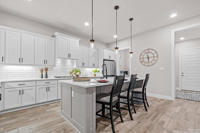 kitchen with white cabinetry, backsplash, a kitchen island with sink, and decorative light fixtures