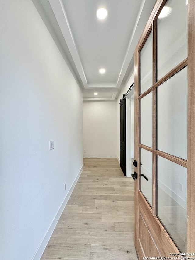 hall with a tray ceiling, a barn door, and light wood-type flooring