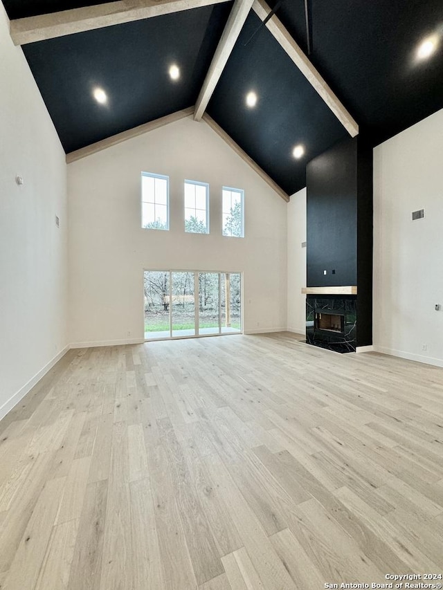 unfurnished living room with a high end fireplace, light hardwood / wood-style floors, beam ceiling, and high vaulted ceiling