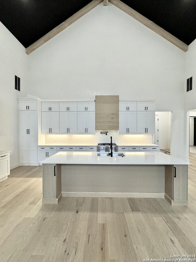 kitchen featuring a large island with sink, white cabinetry, and high vaulted ceiling