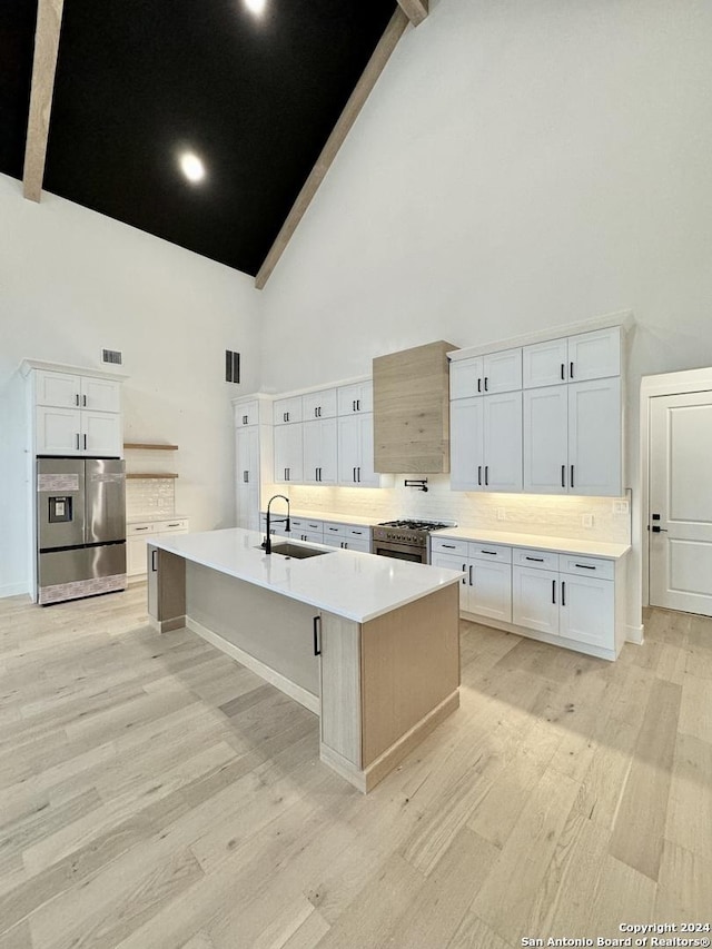 kitchen featuring sink, stainless steel appliances, high vaulted ceiling, a large island with sink, and white cabinets