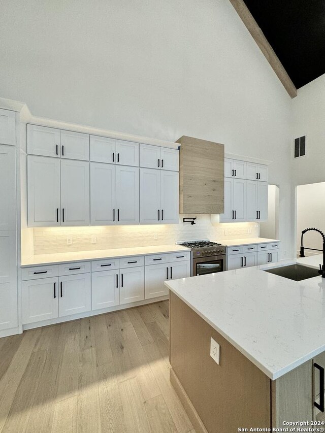 kitchen with light stone counters, stainless steel range, sink, high vaulted ceiling, and white cabinetry