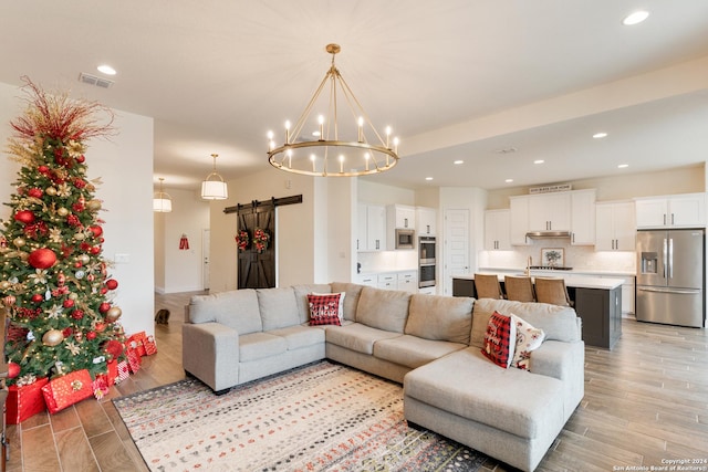 living room with a barn door, sink, light hardwood / wood-style flooring, and an inviting chandelier