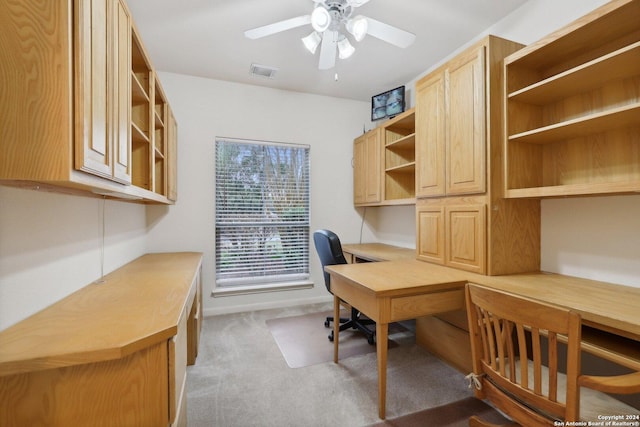 carpeted home office with ceiling fan and built in desk