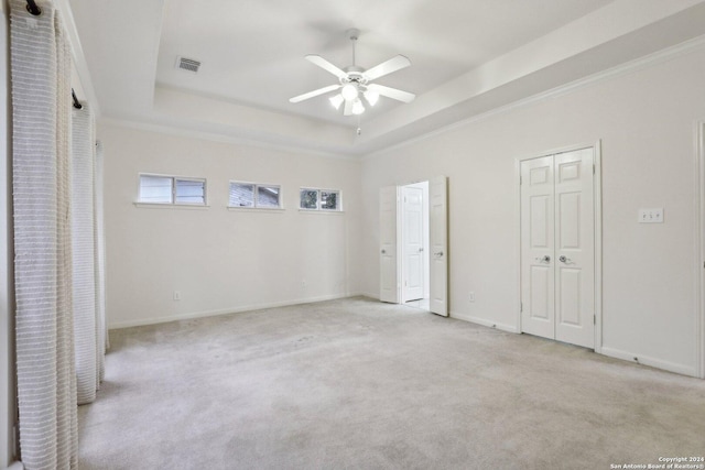 unfurnished bedroom featuring ceiling fan, light colored carpet, ornamental molding, and a tray ceiling