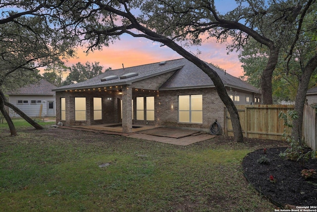 back house at dusk with a lawn and a patio area