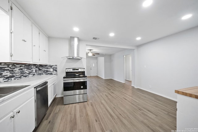 kitchen with decorative backsplash, stainless steel appliances, wall chimney range hood, light hardwood / wood-style flooring, and white cabinets