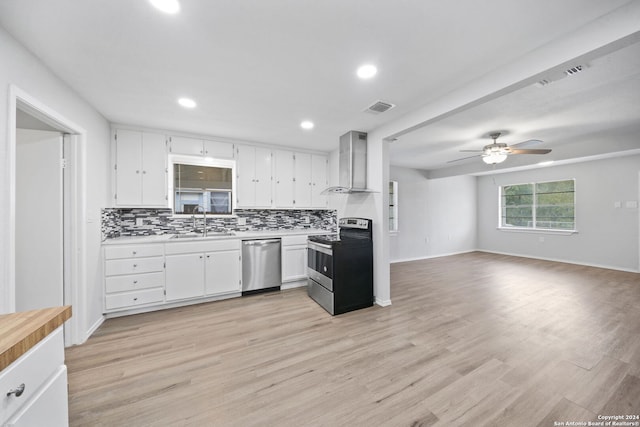 kitchen featuring wall chimney range hood, sink, light hardwood / wood-style flooring, appliances with stainless steel finishes, and white cabinetry