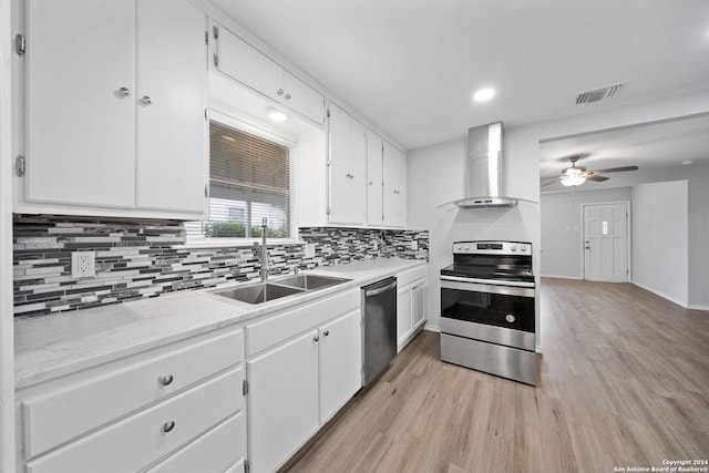 kitchen with wall chimney exhaust hood, stainless steel appliances, sink, light hardwood / wood-style flooring, and white cabinets