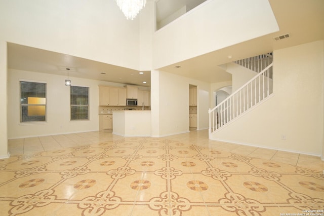 unfurnished living room featuring a notable chandelier, light tile patterned flooring, and a high ceiling