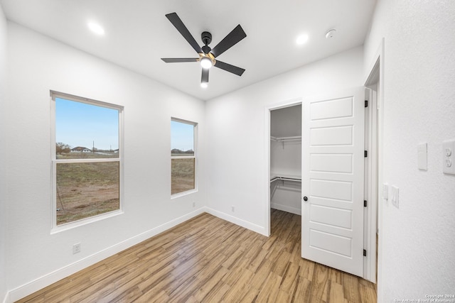 unfurnished bedroom with ceiling fan, light wood-type flooring, a walk in closet, and a closet