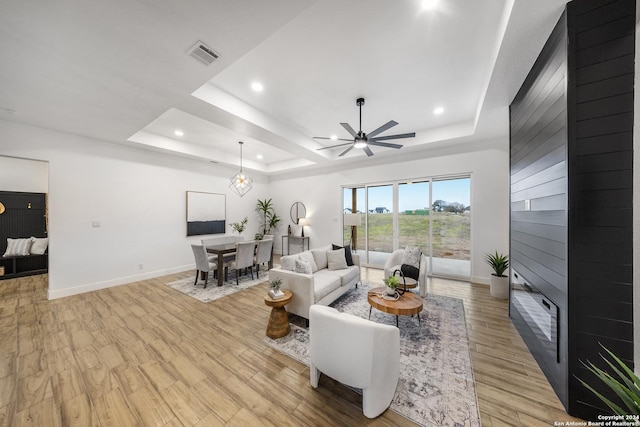 living room featuring light hardwood / wood-style floors, ceiling fan, and a tray ceiling