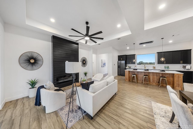 living room with a raised ceiling, a large fireplace, ceiling fan, and light hardwood / wood-style flooring