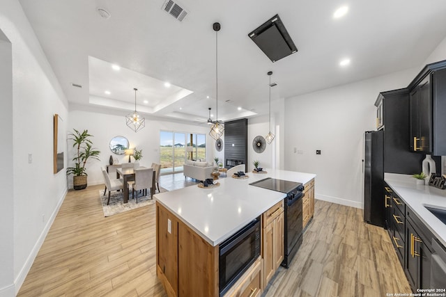 kitchen featuring ceiling fan, hanging light fixtures, light hardwood / wood-style flooring, a kitchen island, and black appliances