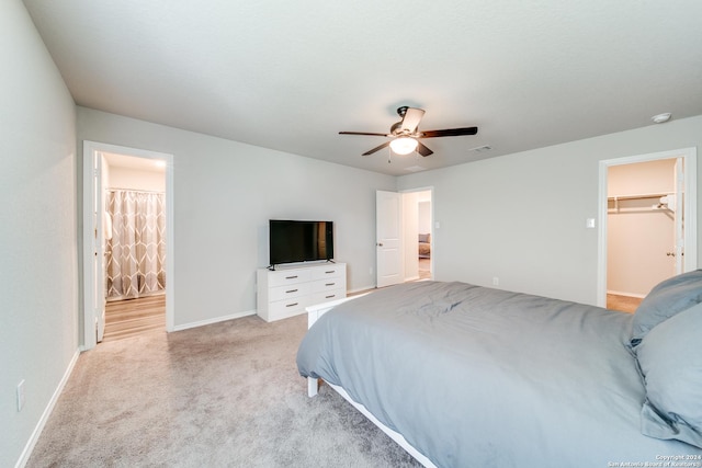 bedroom with light carpet, a walk in closet, ensuite bath, ceiling fan, and a closet