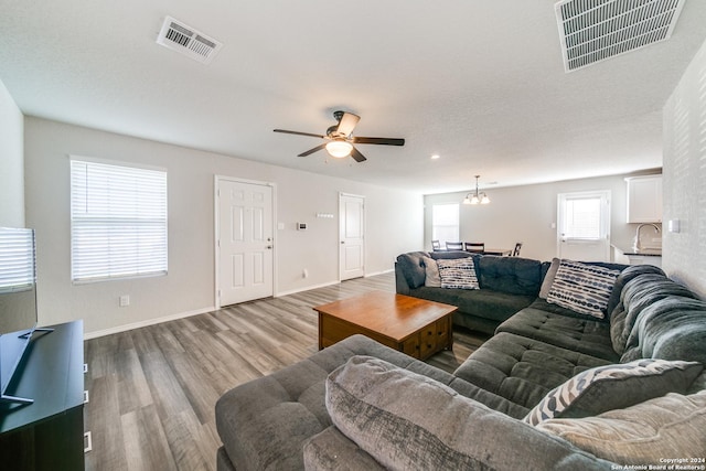 living room with ceiling fan with notable chandelier, a textured ceiling, and light wood-type flooring