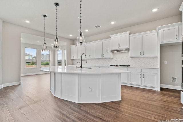 kitchen with sink, decorative light fixtures, white cabinetry, hardwood / wood-style flooring, and a kitchen island with sink