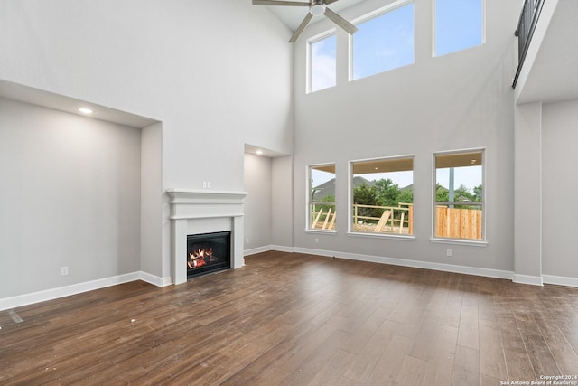 unfurnished living room featuring a towering ceiling, ceiling fan, and dark wood-type flooring