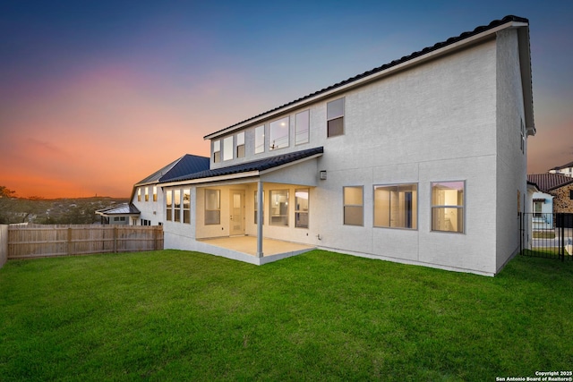 back house at dusk featuring a yard and a patio area