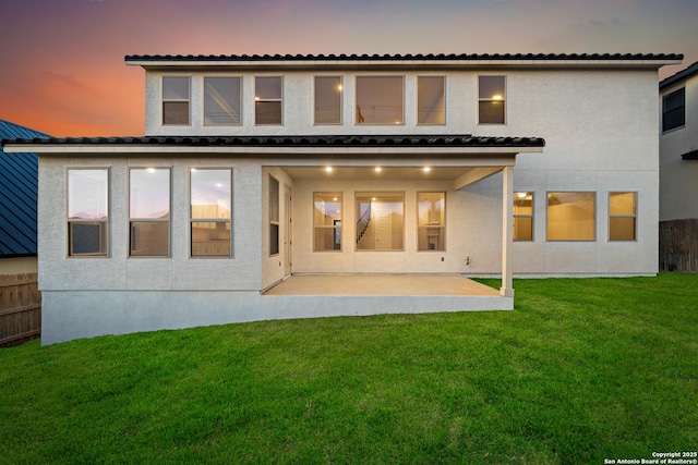 back house at dusk featuring a lawn and a patio area