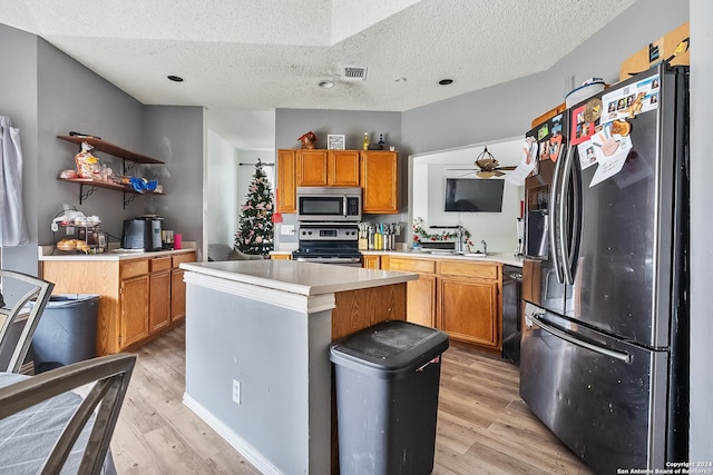 kitchen with appliances with stainless steel finishes, a textured ceiling, light hardwood / wood-style floors, and a center island