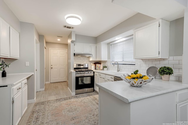 kitchen featuring stainless steel gas range oven, white cabinets, sink, light hardwood / wood-style floors, and kitchen peninsula