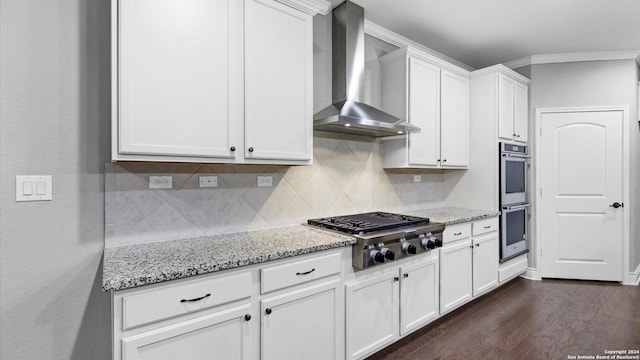 kitchen featuring wall chimney exhaust hood, light stone counters, dark hardwood / wood-style floors, white cabinets, and appliances with stainless steel finishes