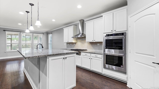 kitchen featuring white cabinetry, wall chimney exhaust hood, stainless steel appliances, dark hardwood / wood-style flooring, and a kitchen island with sink