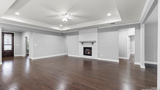 unfurnished living room featuring ornamental molding, a raised ceiling, ceiling fan, a fireplace, and dark hardwood / wood-style floors