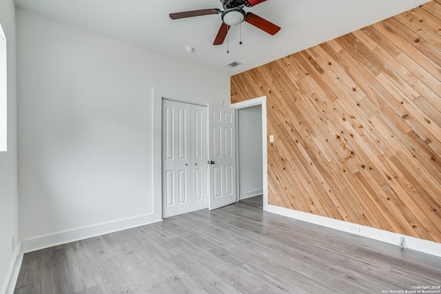 empty room featuring wood walls, light hardwood / wood-style flooring, and ceiling fan