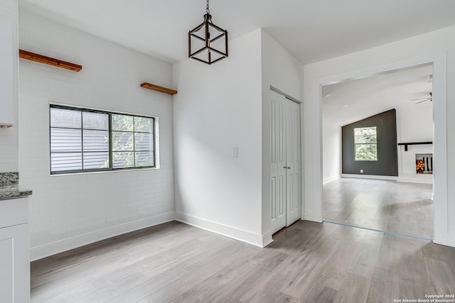 interior space with a wealth of natural light, ceiling fan, brick wall, and light wood-type flooring