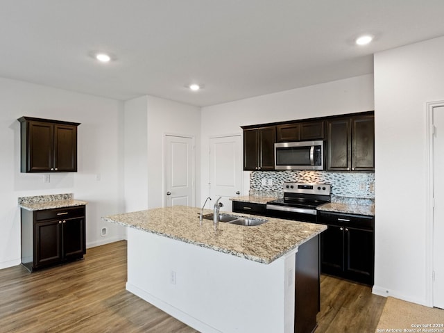 kitchen with light stone countertops, stainless steel appliances, a kitchen island with sink, dark wood-type flooring, and sink