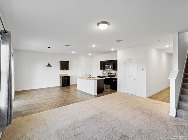 kitchen featuring pendant lighting, a kitchen island with sink, decorative backsplash, appliances with stainless steel finishes, and wood-type flooring