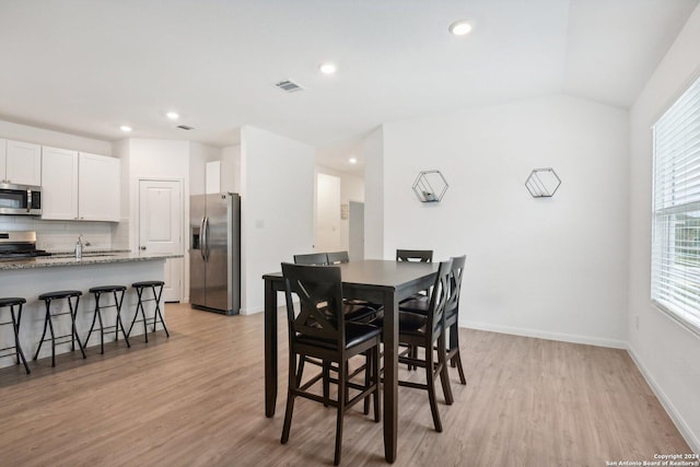 dining area with vaulted ceiling, light hardwood / wood-style flooring, and sink