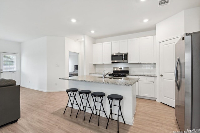 kitchen with white cabinets, an island with sink, light hardwood / wood-style floors, and appliances with stainless steel finishes